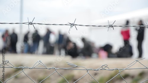 Barbed wire in refugee camp. Migrants behind chain link fence in camp. Group of people behind fence. Concept of prison, freedom, barrier, security and migration. Refugees on their way to EU.