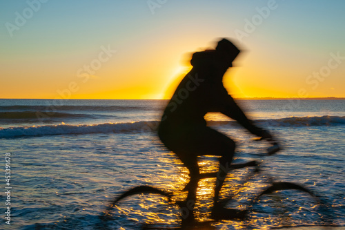 Blurred image of cyclist on beach back lit by sunrise on distant horizon © Brian Scantlebury