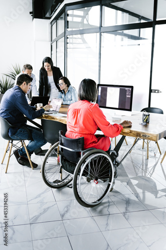 Mexican business people and disabled woman in wheelchair working on business strategies at office desk in Mexico City photo