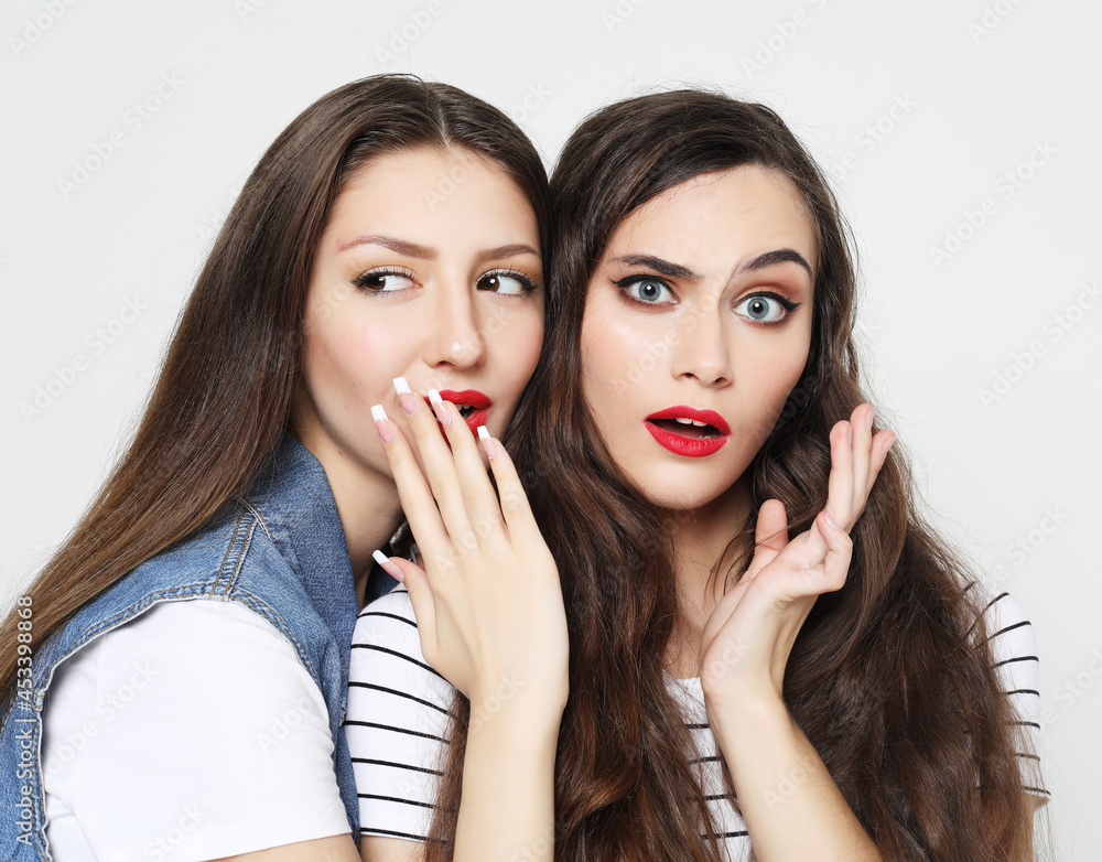 Portrait of two happy young women sharing secrets isolated over white background Portrait of two happy young women sharing secrets isolated over white background