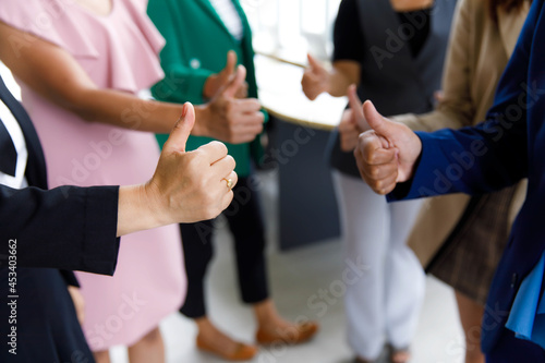 Unrecognizable unidentified female officer staff in business suit show thumb up while others standing ovation side by side applauding hands showing warm greeting celebration in blurred background