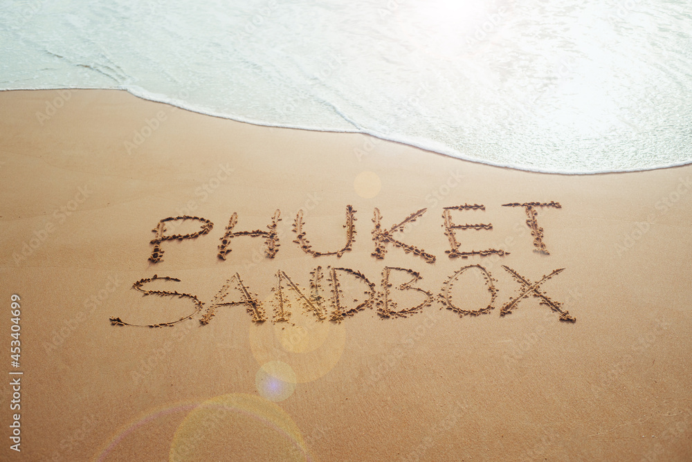 Fototapeta premium Phuket Sandbox text written in the sand on the beach in Phuket, Thailand with incoming wave