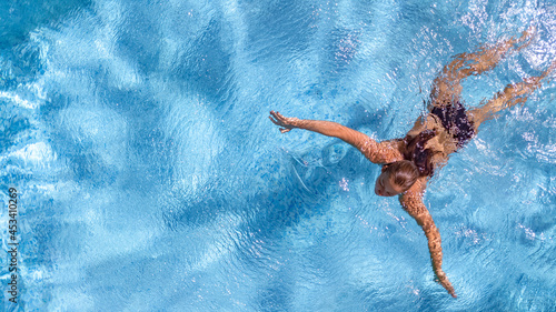 Active young girl in swimming pool aerial drone view from above  young woman swims in blue water pool  tropical vacation on holiday resort  