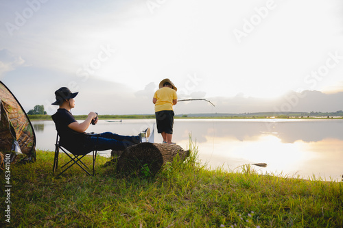 happy family Young Asian traveler and son camping together father and son in front of a camping tent in the evening against a lake or river background. Young Asian man enjoying camping