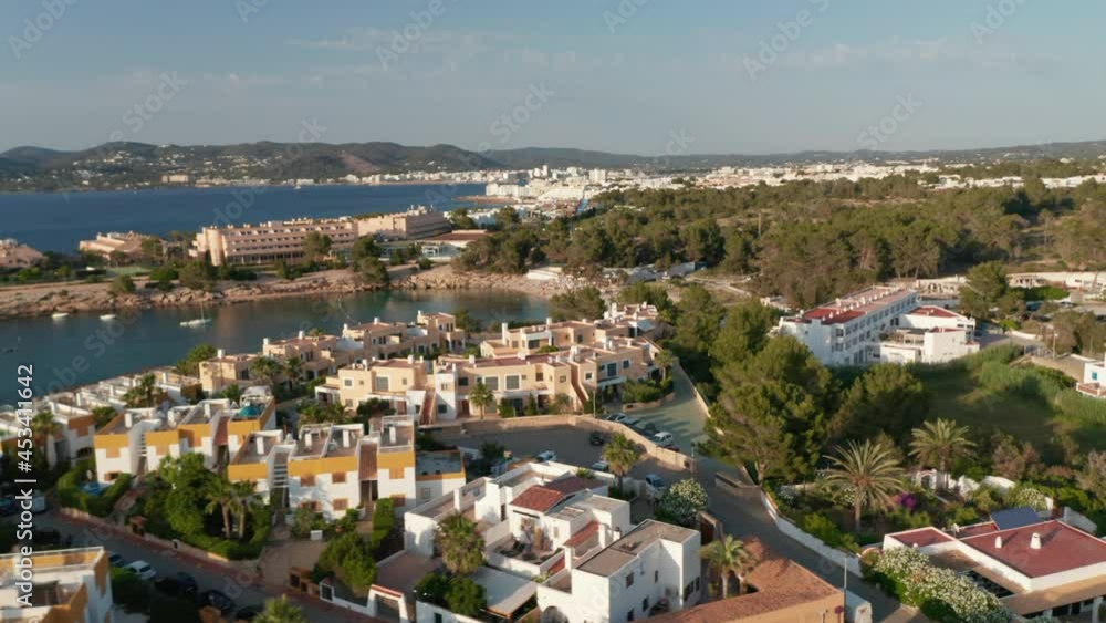 Aerial circular motion view of rooftop of beautiful houses near the beach and shore with boats and yachts parked surrounded by ocean and mountain in Ibiza in Spain during an early morning Aerial circular motion view of rooftop of beautiful houses near the beach and shore with boats and yachts parked surrounded by ocean and mountain in Ibiza in Spain during an early morning