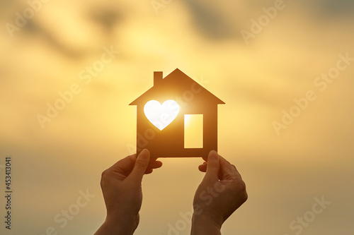 Woman holding a wooden house in front of the sun