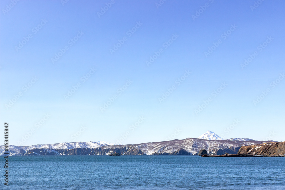 Russia, Kamchatka, Zavoiko village. An abandoned warship, covered with rust, lies aground . In the background there is a volcano and hills covered with snow.