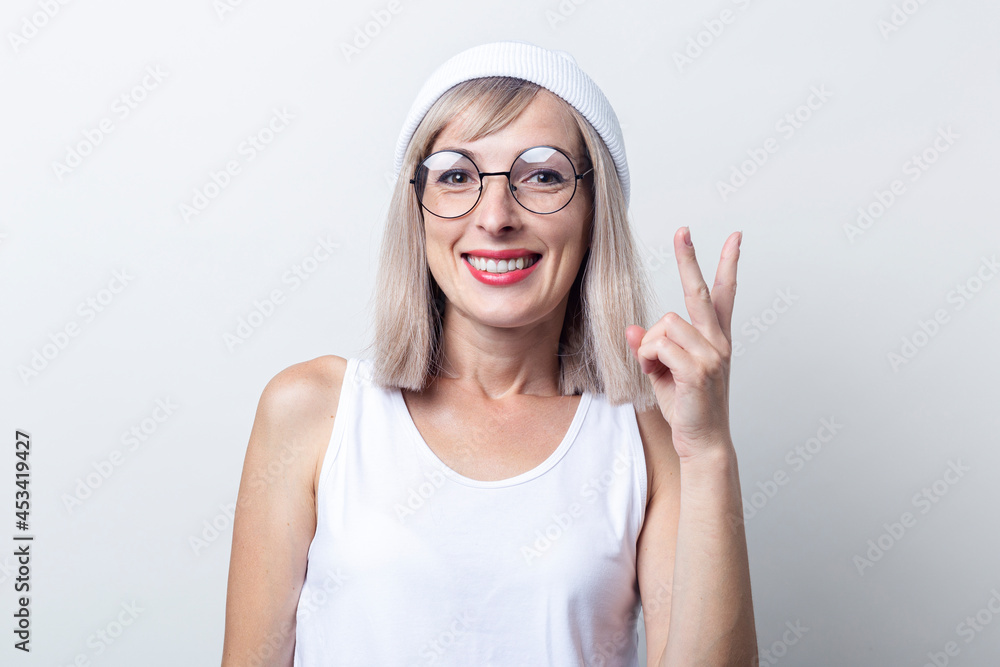 Smiling young woman showing two fingers a victory sign on a light background Smiling young woman showing two fingers a victory sign on a light background