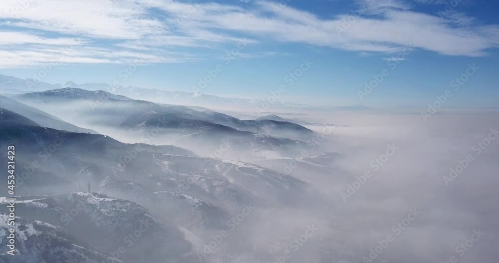 Fog rises on the slopes of the mountains. From above, white clouds, blue sky and snow hills. The winter land was covered with fog. A light layer of fog. Fog rises on the slopes of the mountains. From above, white clouds, blue sky and snow hills. The winter land was covered with fog. A light layer of fog.