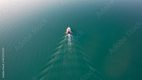 Obraz na płótnie A white boat sails on Lake Balkhash at sunset. A beautiful long train on the water from the motor. The sky gradient is from orange to blue. Smooth water. Travel on a speed bot. Bertys Bay. Kazakhstan w salonie