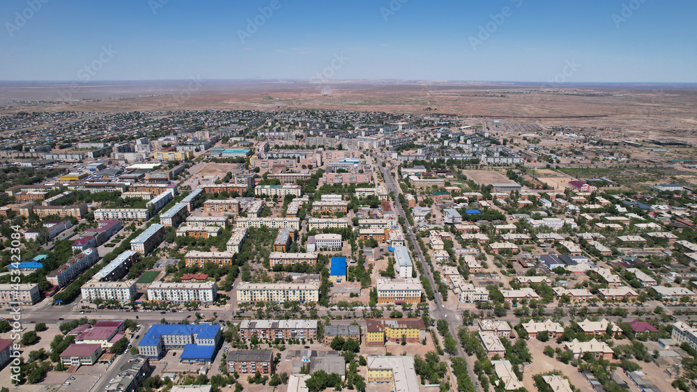 Drone view of the small town of Balkhash. The city is located on the shore of a lake. Low houses, free streets and roads. Green trees grow and there are sports grounds. There is a steppe around city