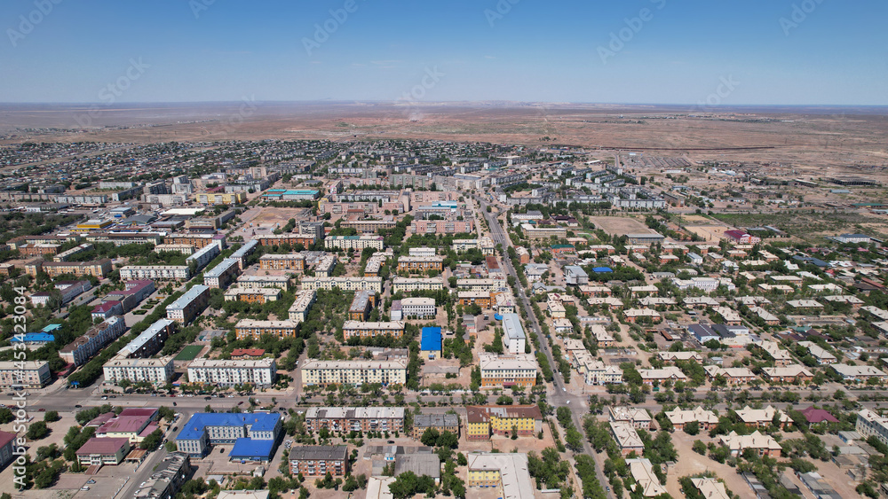 Obraz premium Drone view of the small town of Balkhash. The city is located on the shore of a lake. Low houses, free streets and roads. Green trees grow and there are sports grounds. There is a steppe around city