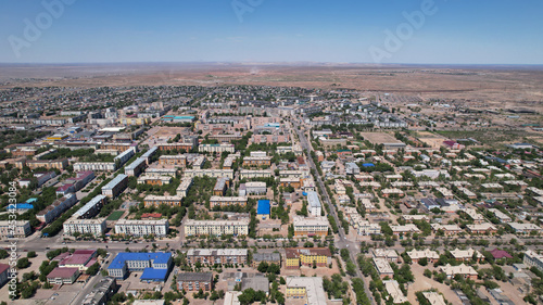 Drone view of the small town of Balkhash. The city is located on the shore of a lake. Low houses, free streets and roads. Green trees grow and there are sports grounds. There is a steppe around city