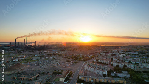 An epic sunset with a view of the smoking factory and the city. The embankment of Lake Balkhash. Low houses are standing and there are few trees. The pipes from the factory are smoking. Kazakhstan © SergeyPanikhin
