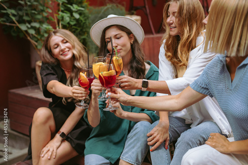 Group of female friends cheers their drinks together, celebrating the first day of vacation.