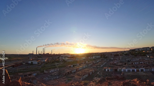 An epic sunset with a view of the smoke of the factory. There are garages and small houses. Near the beach of Lake Balkhash. There are many swifts and different birds flying. Ecology. Air pollution © SergeyPanikhin