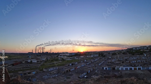 An epic sunset with a view of the smoke of the factory. There are garages and small houses. Near the beach of Lake Balkhash. There are many swifts and different birds flying. Ecology. Air pollution