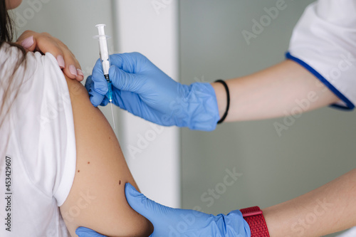 Close-up of female doctor in protective gloves holding syringe making covid 19 vaccination. Women getting injection in shoulder. Vaccine clinical trials concept  corona virus