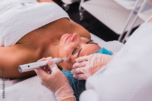 Cosmetologist making mesotherapy treatment with dermapen on face of woman in the aesthetic center photo