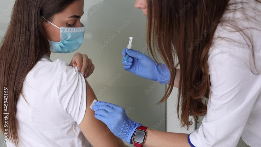 Woman in medical face mask getting Covid-19. Flu vaccine at the hospital. Professional nurse giving antiviral injection to female patient. Vaccination, disease prevention concept. Close-up of
