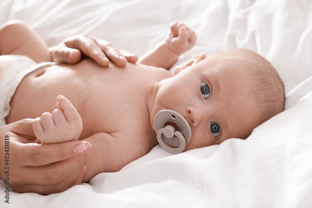 Mother and her cute little baby with pacifier on bed, closeup Mother and her cute little baby with pacifier on bed, closeup