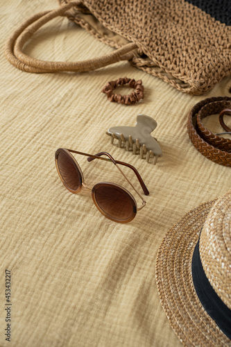 Fashion female beach accessories on yellow muslin cloth. Belt, straw bag, sunglasses, hat, sunglasses. Aesthetic luxury boho concept for travel blog, social media