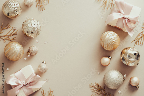Christmas frame made of golden balls, decorative branches, gift boxes over beige background. Flat lay, top view. Xmas banner mockup with copy space