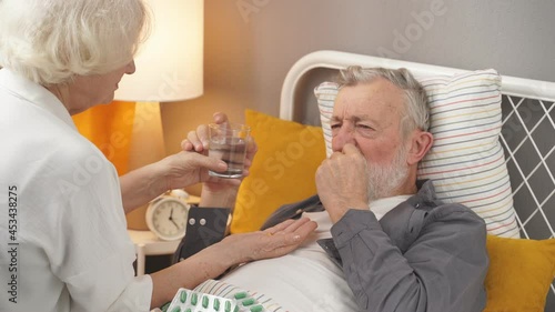 Aged female concerned with health condition of husband, checking fever temperature lying on bed. photo