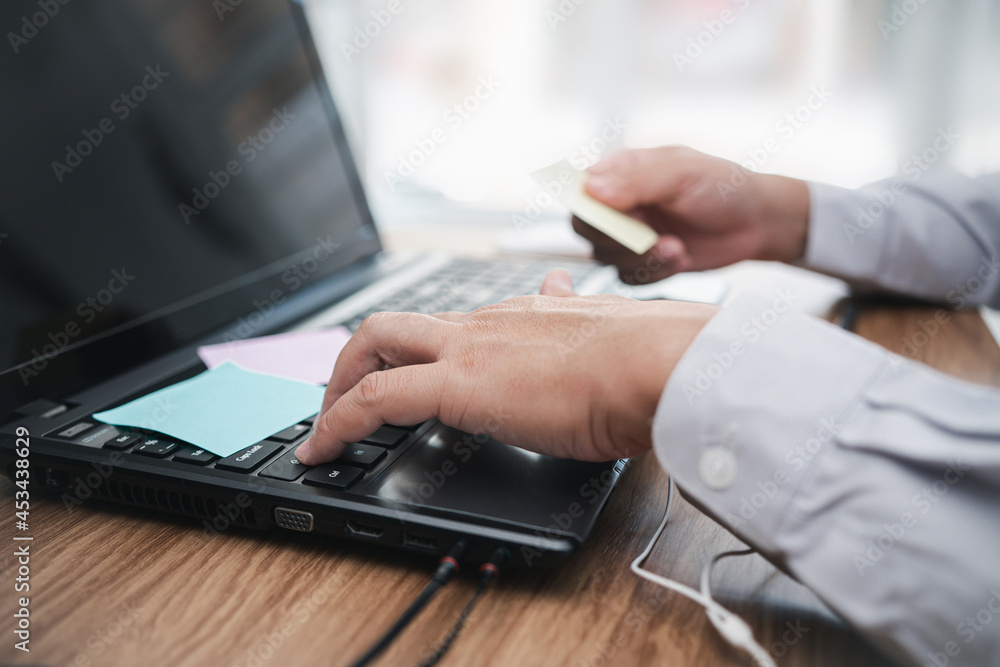 A man typing on keyboard laptop and hold a post it note paper  written for memory and working in office