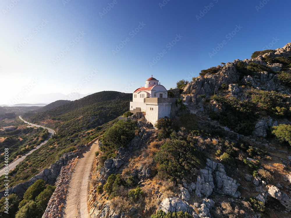 a panoramic view of the white stone church against the backdrop of mountains and olive groves of Crete filmed from a drone 
