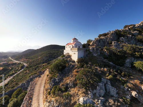 a panoramic view of the white stone church against the backdrop of mountains and olive groves of Crete filmed from a drone 
