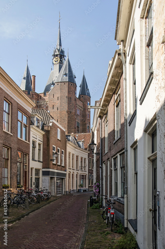 Fototapeta premium Zwolle, The Netherlands, August 9, 2021: Narrow street in the old town with the tower of Sassenpoort gate rising above the brick and plaster facades.