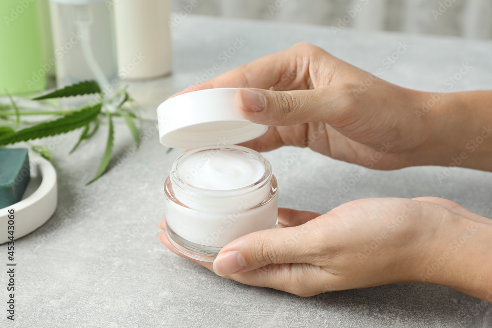 Woman holding jar of hemp cream at light table, closeup. Natural cosmetics Woman holding jar of hemp cream at light table, closeup. Natural cosmetics