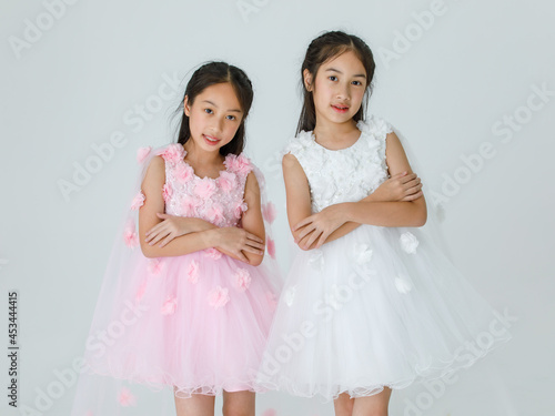 Portrait isolated studio shot of two little Asian ballerina kids in pink and white beautiful roses flowers ballet dress red shoes and high heels smile look at camera  together