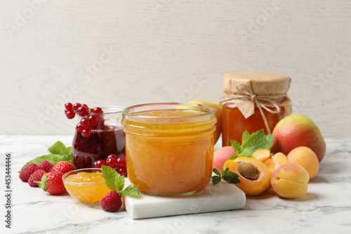 Jars with different jams and fresh fruits on white marble table