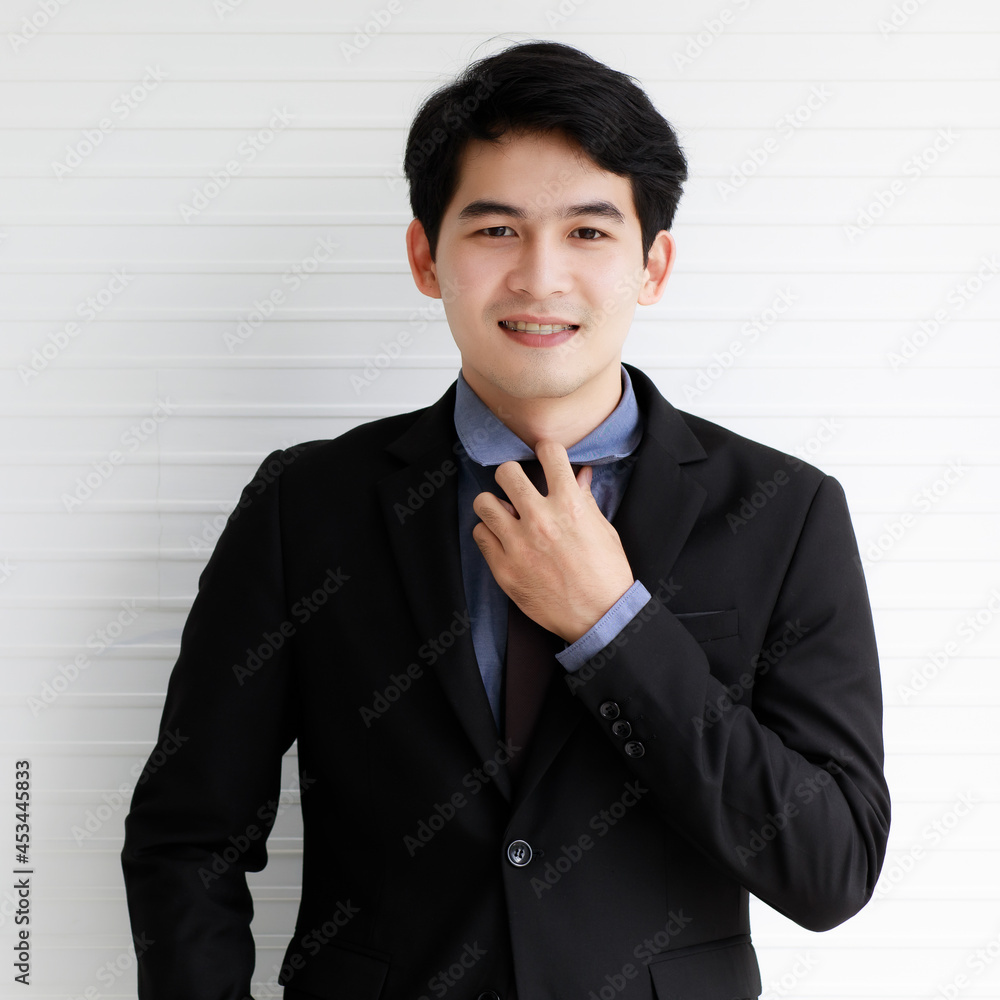 Portrait of an asian handsome business man wearing formal black suit, tie his necktie, smiling with confidence and happiness and standing on white background. Portrait of an asian handsome business man wearing formal black suit, tie his necktie, smiling with confidence and happiness and standing on white background.