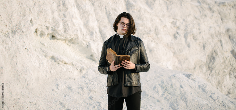 Young priest portrait outside at sunset. He is wearig eye glasses and roman collar shirt and a leather jacket. Young priest portrait outside at sunset. He is wearig eye glasses and roman collar shirt and a leather jacket.