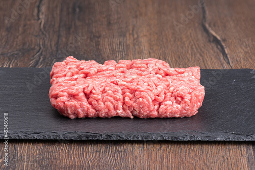 Minced meat on a slate stone board over a wooden background.