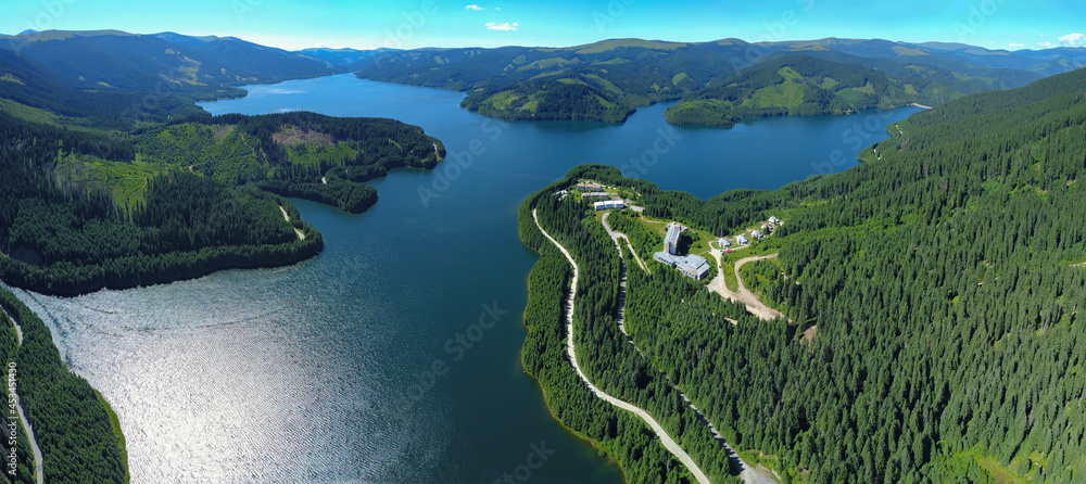 Fototapeta premium Panoramic view above Vidra Lake. The lake is located in a mountainous area, surrounded by coniferous forests. Vidra resort is built near the lake. Carpathia, Romania. 