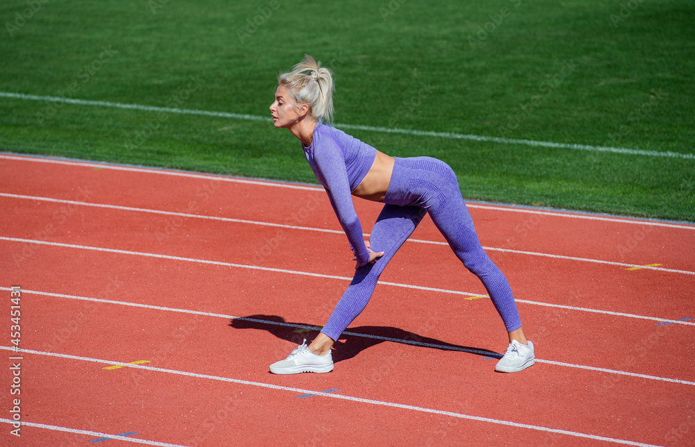 sexy sporty woman stretching and warming up in sportswear on stadium running track, health care