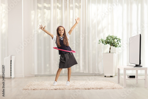 Playful schoolgirl dancing with a hula hoop at home