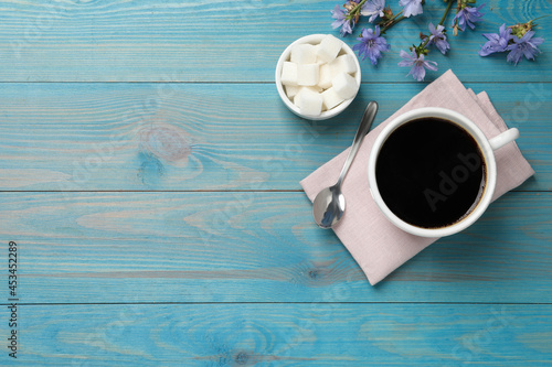 Cup of delicious chicory drink, sugar and flowers on turquoise wooden table, flat lay. Space for text