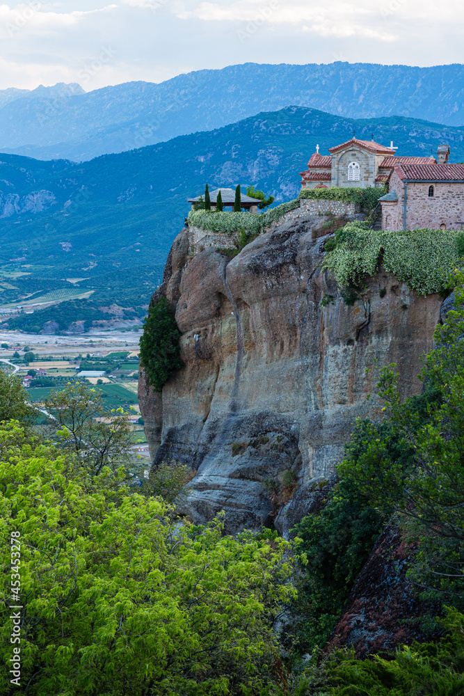 ギリシャ　メテオラの断崖絶壁の岩山の上に建つ聖ステファノス修道院と奇岩群の隙間から覗くカランバカの街並みと後ろに広がるピンドス山脈