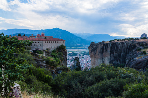 ギリシャ メテオラの断崖絶壁の岩山の上に建つ聖ステファノス修道院と奇岩群の隙間から覗くカランバカの街並みと後ろに広がるピンドス山脈