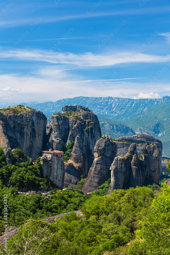 ギリシャ　メテオラの断崖絶壁の岩山の上に建つルサヌ修道院と周りを囲む奇岩群と後ろに広がるピンドス山脈