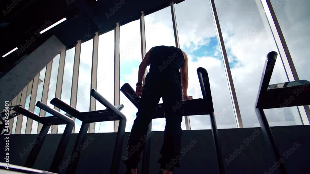 Sportsman on treadmill in gym. Guy in sportswear standing on a treadmill and doing running exercise on window background. Back view from below. Sportsman on treadmill in gym. Guy in sportswear standing on a treadmill and doing running exercise on window background. Back view from below.