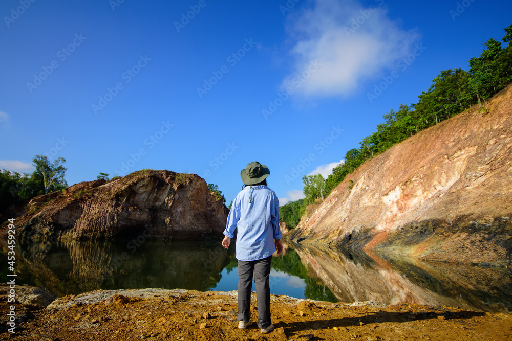 A woman stands on the rocky  watching the beautiful landscape and rocky mountains in the lake.
