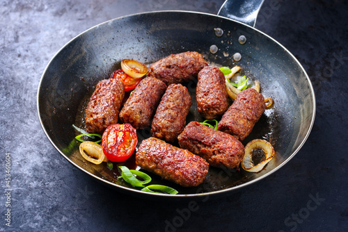 Traditional Croatian cevapi spicy meat ball rolls with tomatoes and onion rings served as close-up in a skillet photo