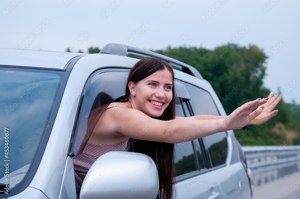 A happy girl with long hair stuck her hands out of the cab of a car on the road, the concept of auto travel