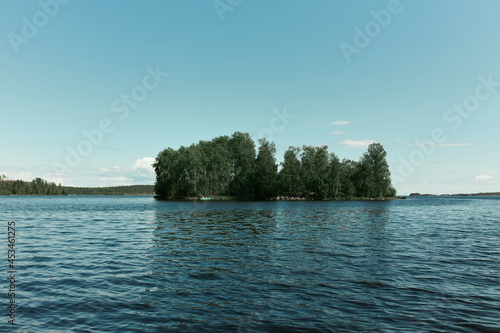 Water walk on sunny summer day. Little wild island covered with small forest reflecting on water surface of deep blue river. Nobody around. Quiet and peaceful place for meditation and relaxation